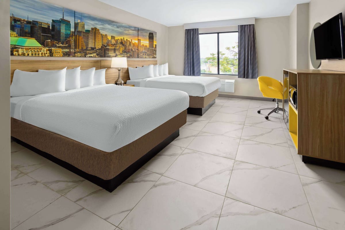 A hotel room with two beds, a desk, a chair, a TV, and a cityscape mural on the wall.