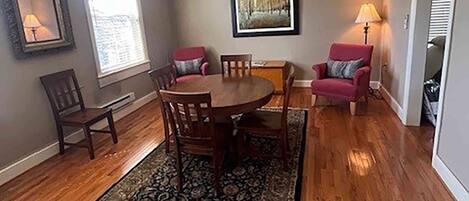 A dining room with a wooden table and chairs, a patterned rug, and two red armchairs.