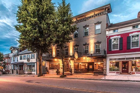A historic building with a large tree in front, multiple storefronts, and a well-lit entrance.