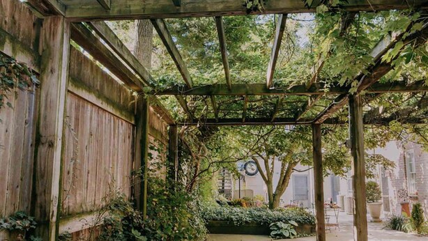 Een houten pergola met een pad van stenen tegels dat leidt naar een zitgedeelte.