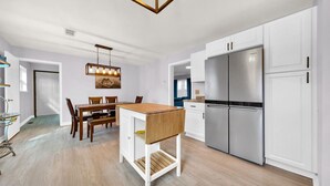 A modern kitchen with white cabinetry, a stainless steel refrigerator, and a wooden dining table. - Walk to bar, shop, and DT (Port Sanilac)