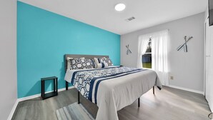 A bedroom with a bed, a small table, a window with curtains, and a wall with a sports equipment decoration. - Walk to bar, shop, and DT (Port Sanilac)