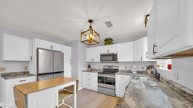 A modern kitchen with white cabinets, stainless steel appliances, a wooden table, and a granite countertop. - Walk to bar, shop, and DT (Port Sanilac)