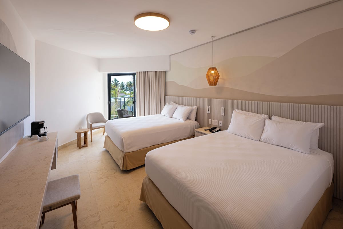 Une chambre d’hôtel avec deux lits, un bureau, une chaise, une petite table et une vue sur l’extérieur.