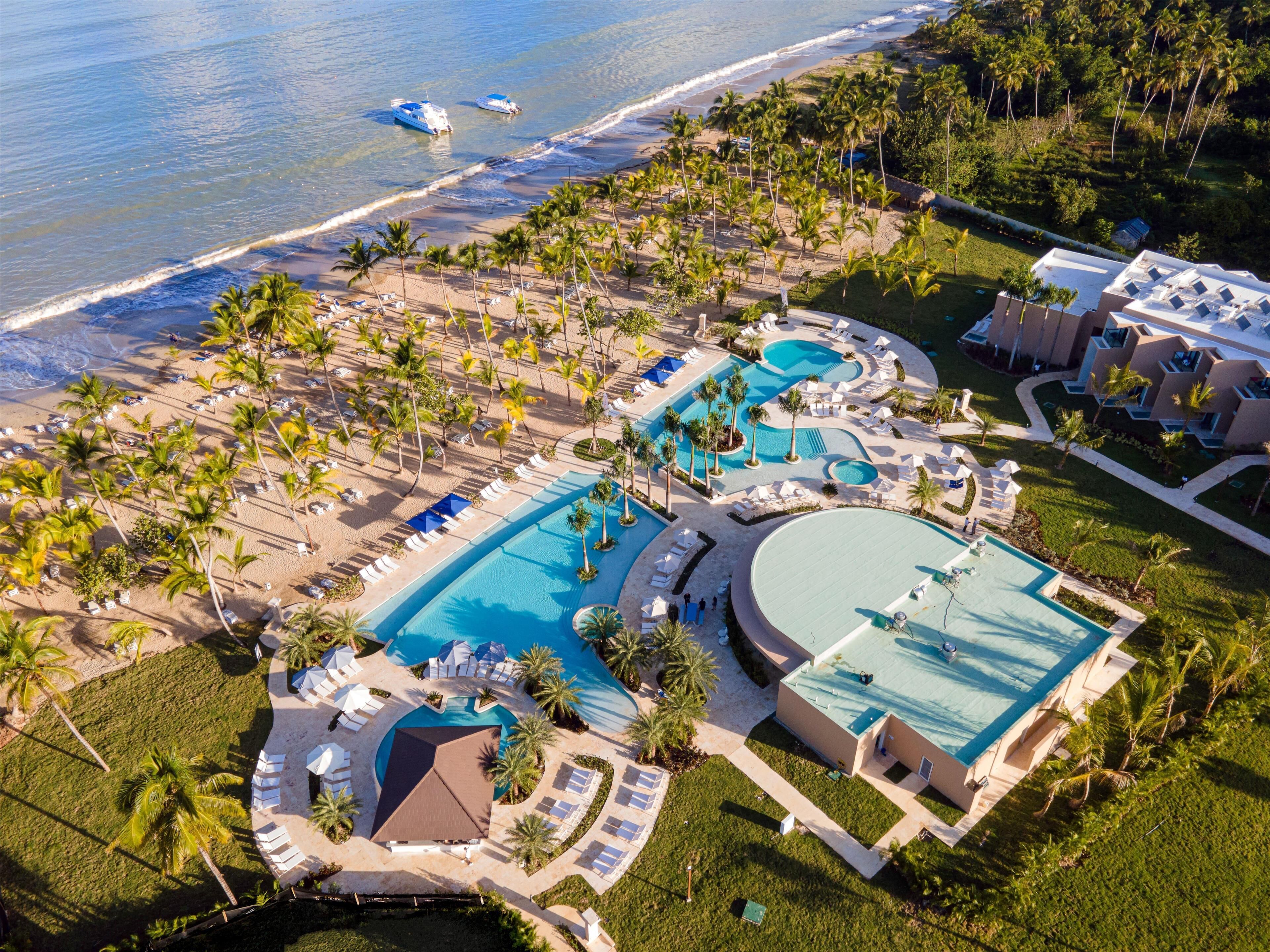 Vista aérea de un resort con varias piscinas, acceso a la playa y palmeras.