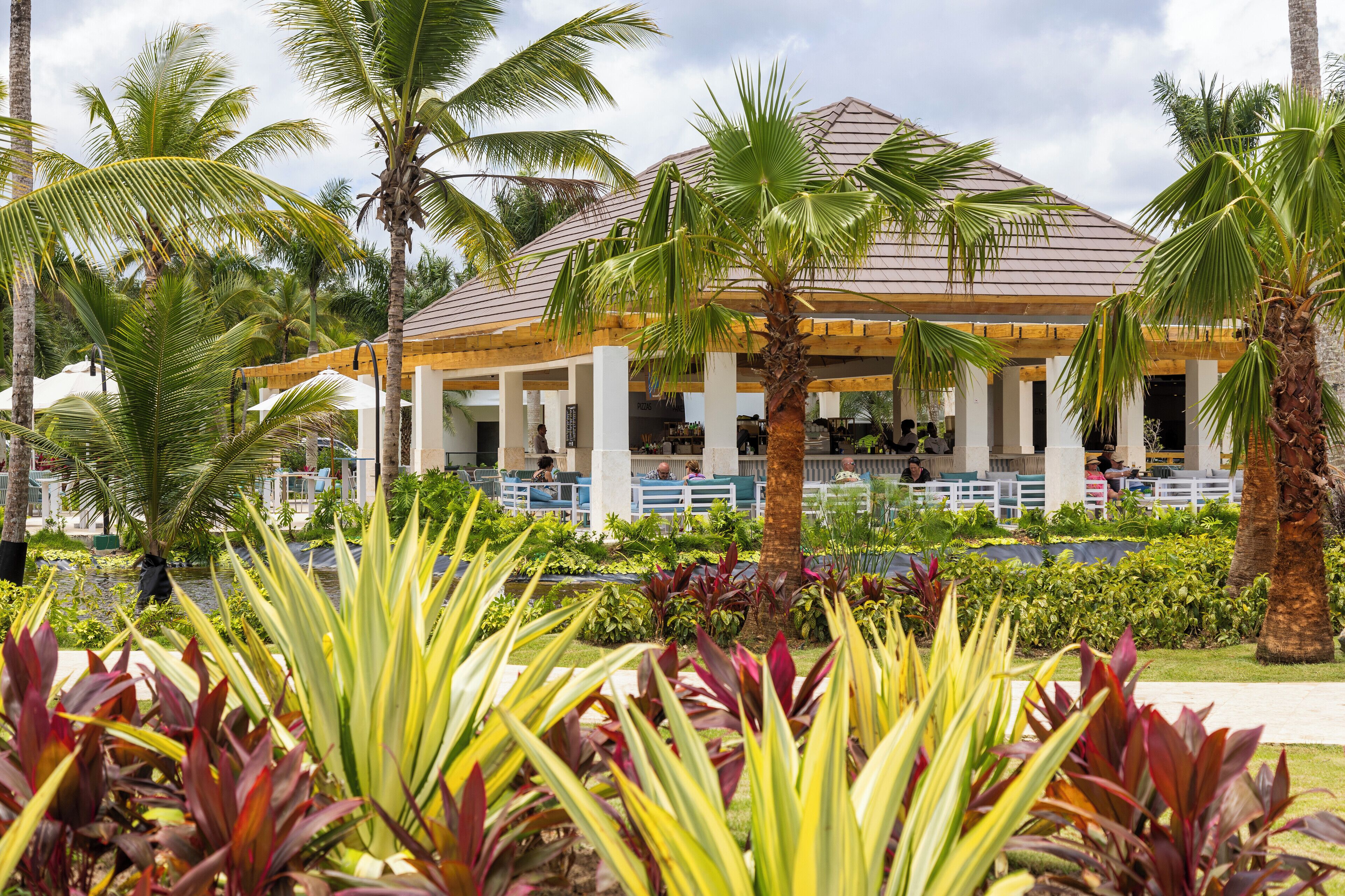 A covered outdoor area with palm trees and a building with a tiled roof.