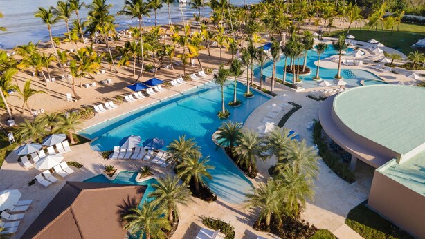 Een resort met een groot zwembad, palmbomen en uitzicht op de oceaan.