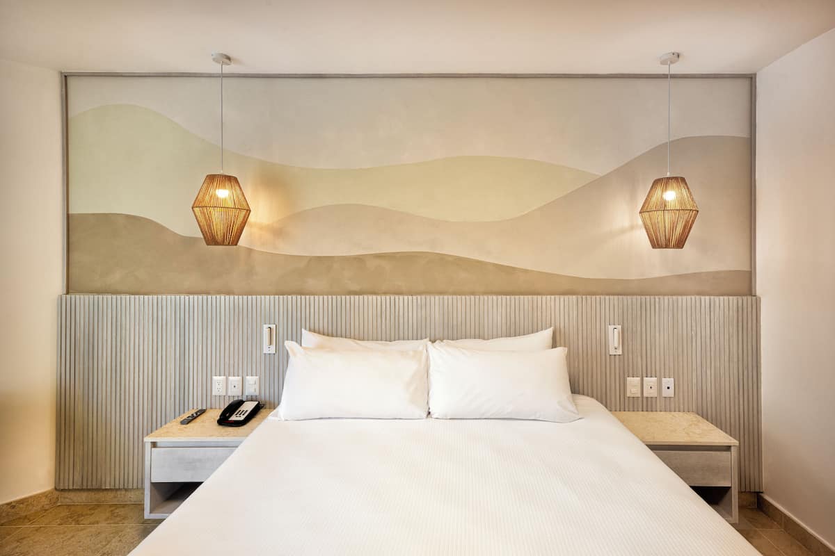 Une chambre d’hôtel avec un grand lit, deux tables de chevet, un téléphone et une œuvre d’art accrochée au mur.