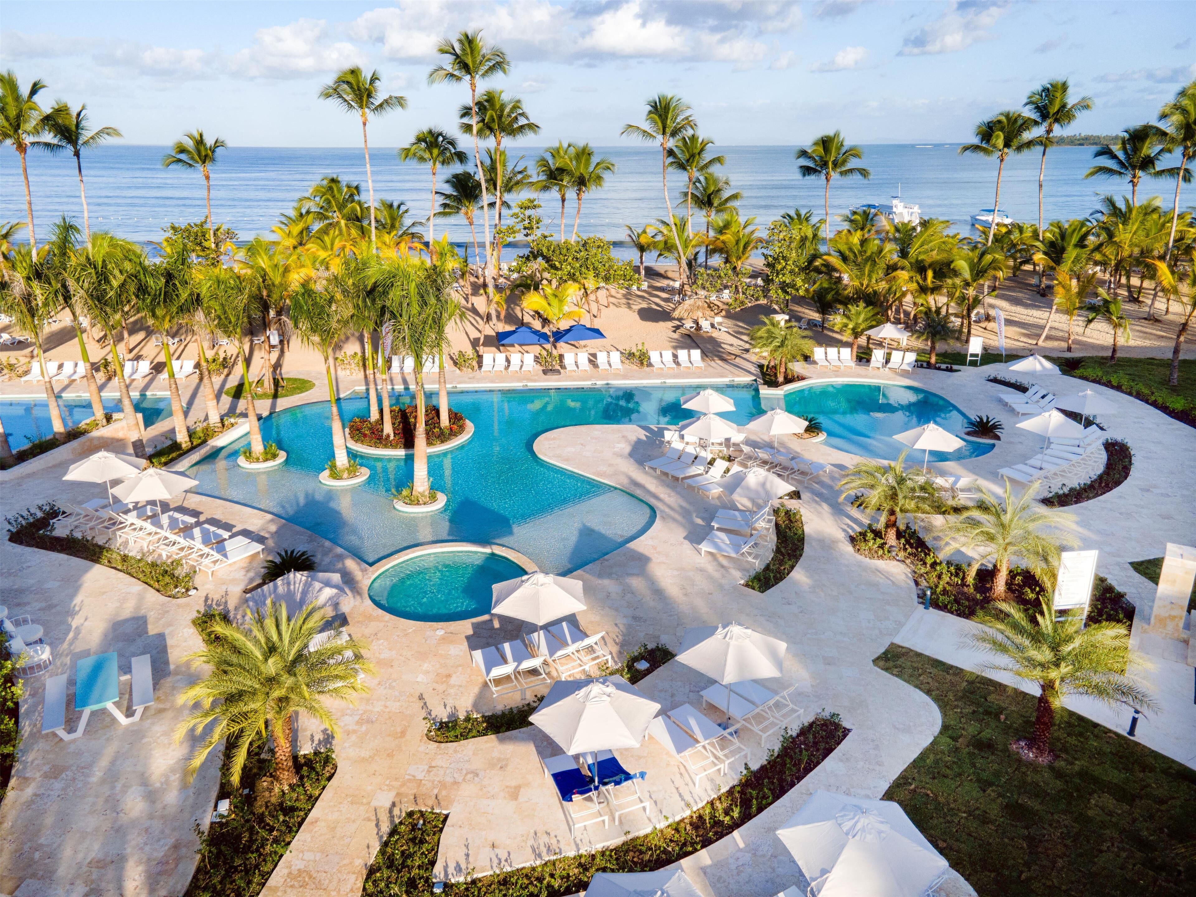 A resort with multiple swimming pools, palm trees, and beach chairs.