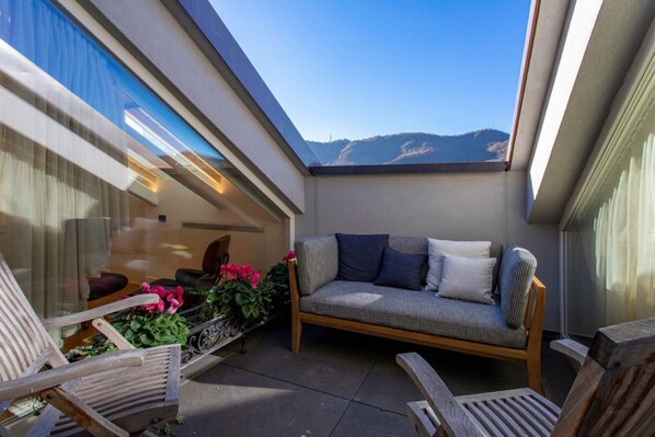 A balcony with a sofa, chairs, and potted plants.