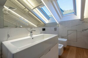 A modern bathroom with a skylight, a large mirror, and a marble wall.
