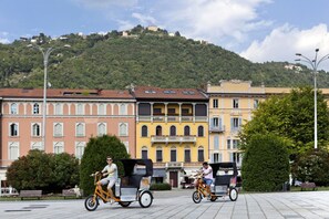 A square with cobblestone pavement, historic buildings with balconies, and a hill in the background.
