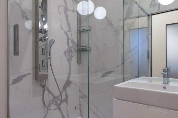Une salle de bain moderne avec une douche à parois de verre, un lavabo blanc et un mur en marbre.