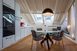 A modern kitchen with a glass dining table, four chairs, a hanging light fixture, and skylights.