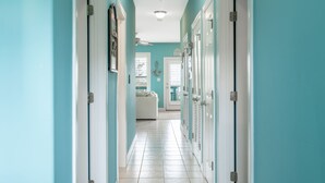A hallway with teal walls, white doors, and a tiled floor leading to a room with a bed and a window.