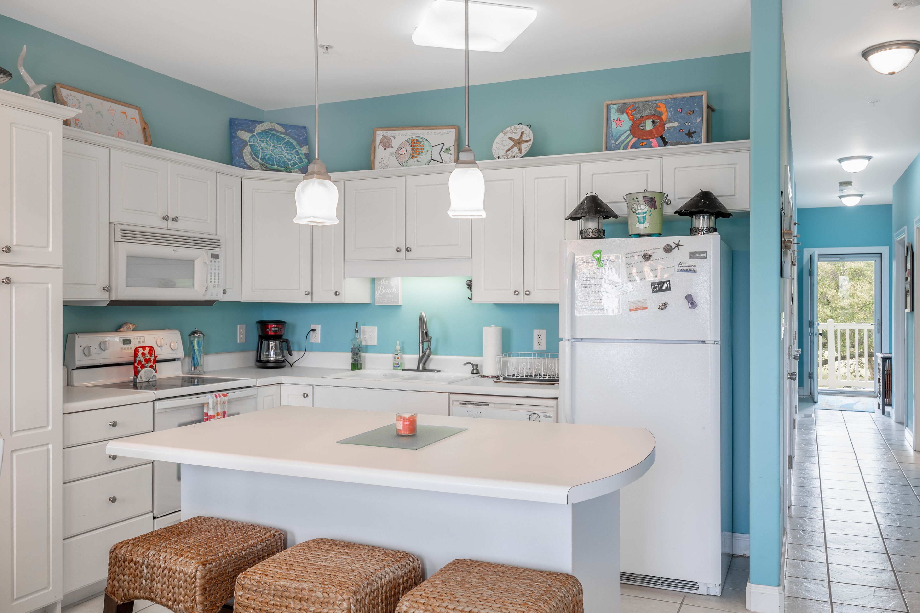 A kitchen with white cabinets, a central island, wicker stools, and various kitchen appliances.