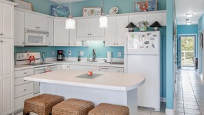 A kitchen with white cabinets, a central island, wicker stools, and various kitchen appliances.