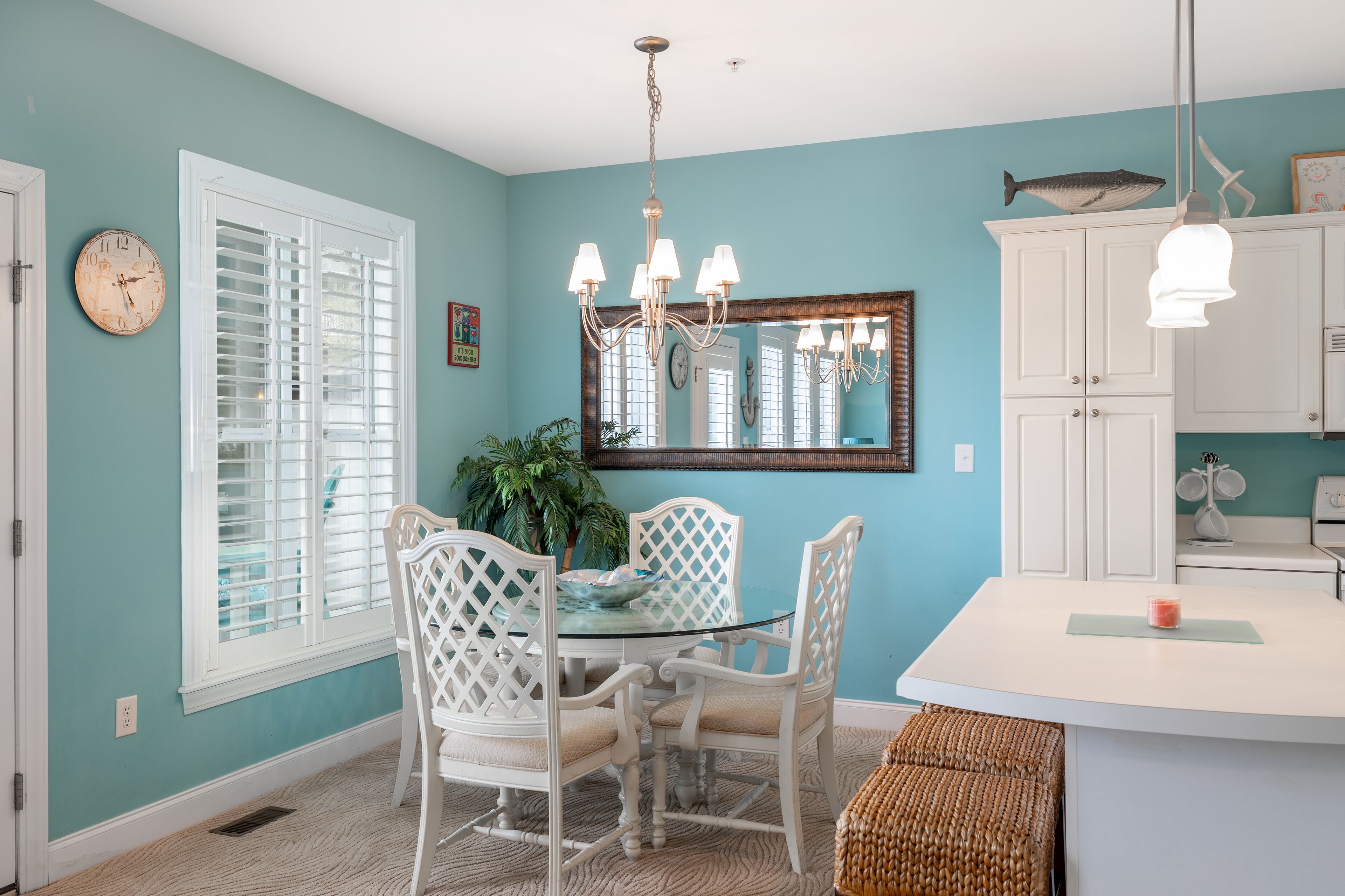 A dining area with a glass table surrounded by white chairs, a chandelier, and a white cabinet with a fish decoration.