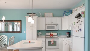 A modern kitchen with white cabinets, a microwave, an oven, and a refrigerator. There is a dining table with chairs and a small island.