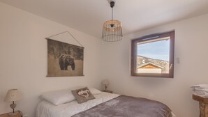 Um quarto com cama, janela com vista, luminária pendente e quadro na parede.