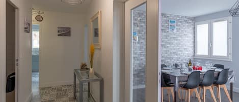 Eine moderne Küche mit Ziegelrückwand, ein Essbereich mit rundem Tisch und Stühlen sowie ein Flur mit gemustertem Boden und einem Konsolentisch mit Glasplatte.