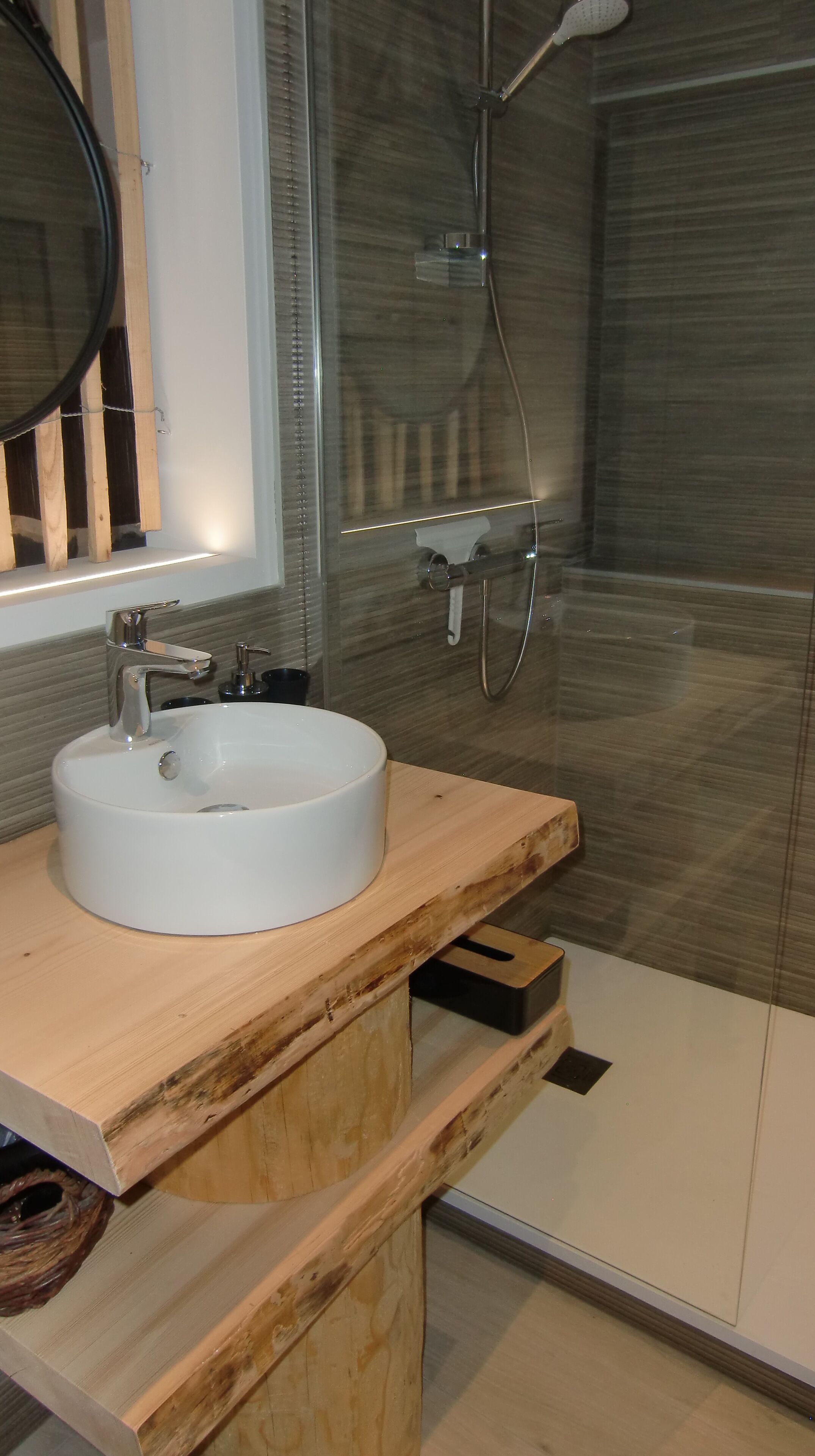 A bathroom with a white sink, wooden vanity, and a glass shower enclosure.