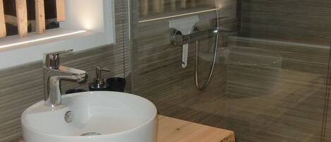 A bathroom with a white sink, wooden vanity, and a glass shower enclosure.