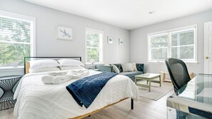A modern bedroom with a bed, a sofa, a desk, and large windows. - Centrally Located in East Quogue, Perfect for Families, Private Pool, Close... (East Quogue)