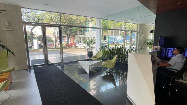 A modern reception area with a glass door entrance, a reception desk, and seating area with chairs and a coffee table. - Gorgeous 2BDRM with A/C - Miraflores (Miraflores)