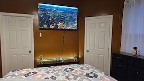 A bedroom with a bed, two doors, a dresser, and a TV mounted on the wall displaying a cityscape.