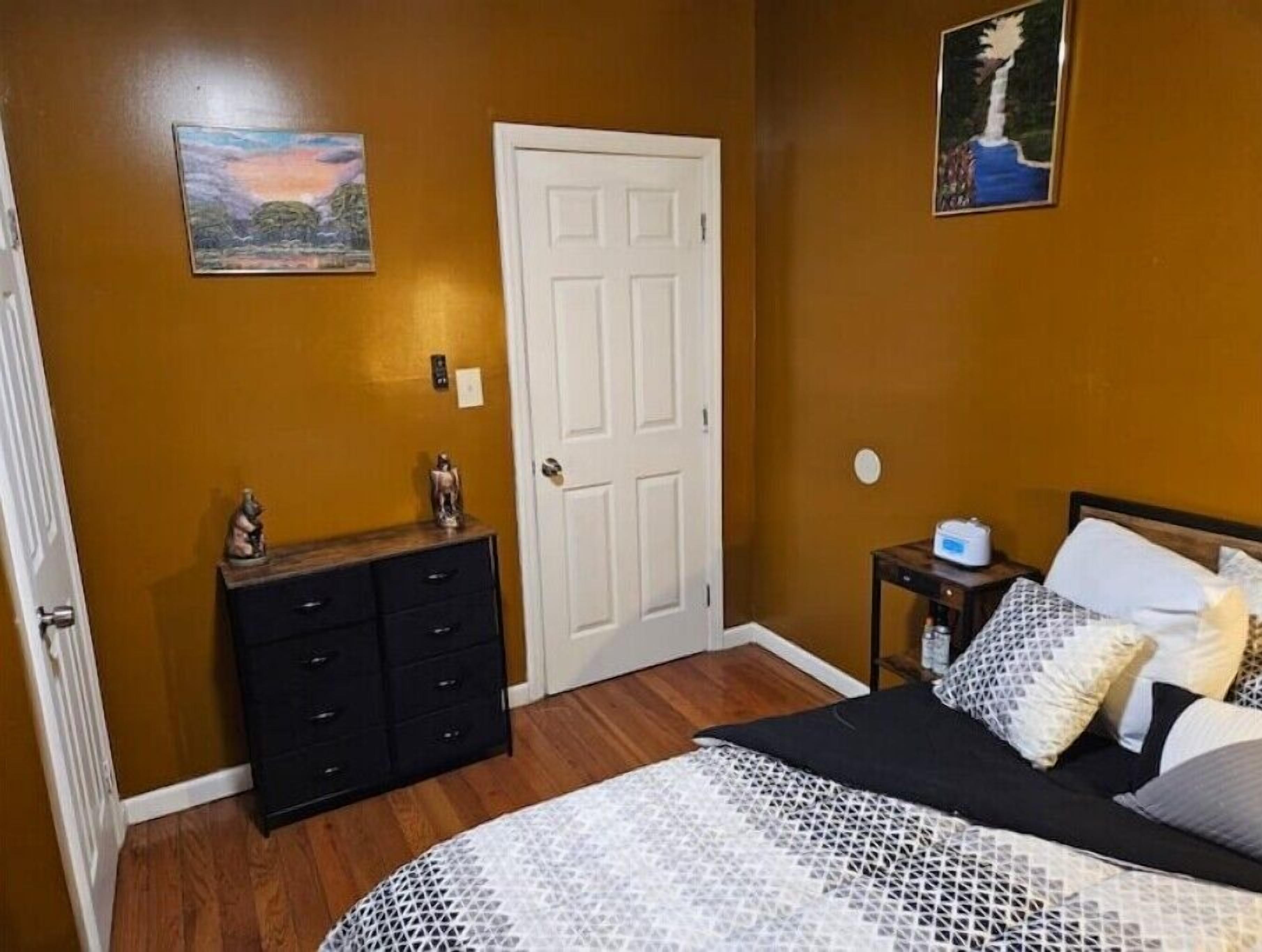 A bedroom with a bed, dresser, nightstand, and two wall art pieces.