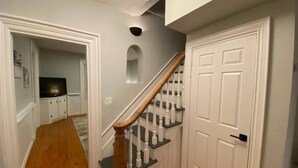Un couloir avec un escalier en bois, des portes blanches et un téléviseur à l’arrière-plan.