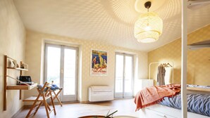 A compact, well-lit room with a bed, a desk, and a chair. There is a large window providing natural light, and a poster is visible on the wall. - Monti 39 (Como)