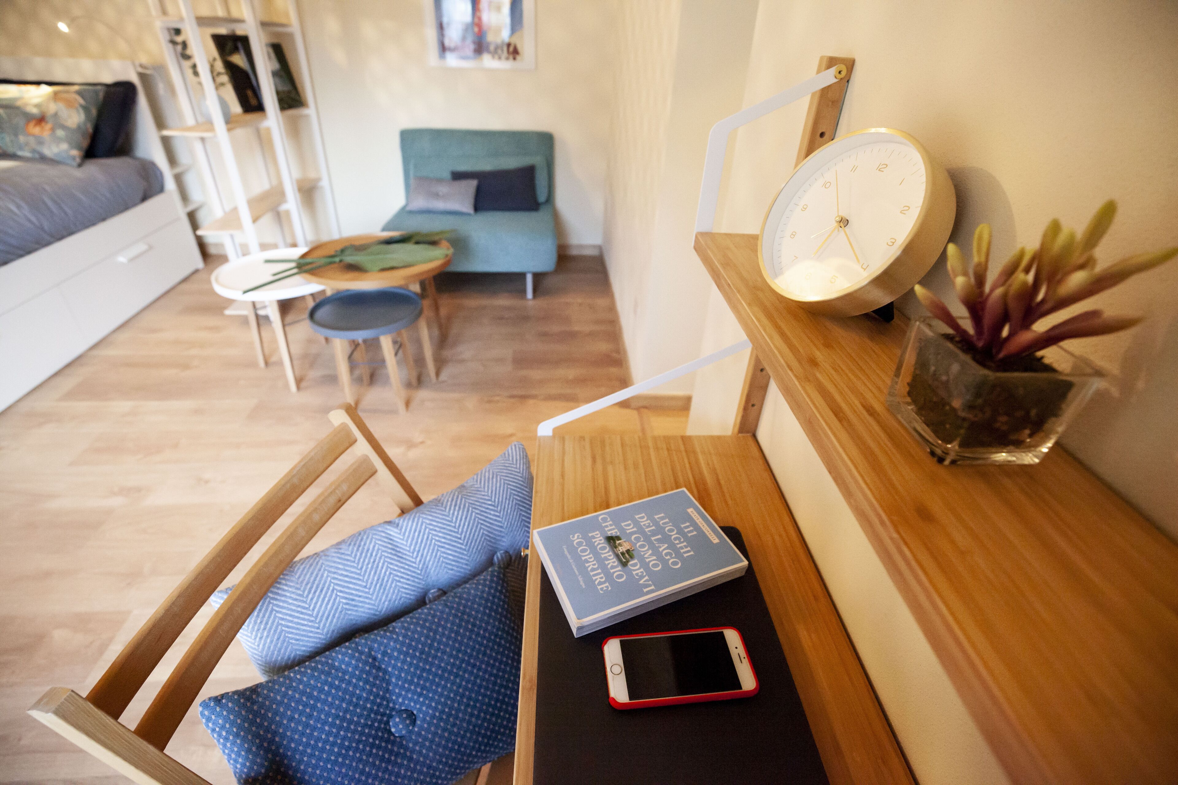A modern living room with a wooden bench, a blue patterned pillow, a book, a smartphone, a clock, and a potted plant.