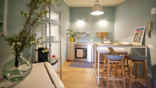A compact kitchen with a central island, a hanging light fixture, and a vase with flowers. - Monti 39 (Como)