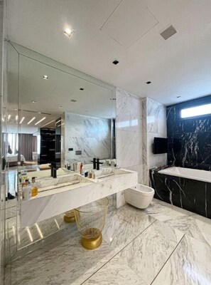 Une salle de bain moderne avec un grand miroir, un revêtement de sol en marbre et un mur d’accent en marbre noir.