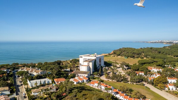 A coastal town with a prominent white building, likely a hotel, surrounded by residential houses with red roofs and lush greenery.