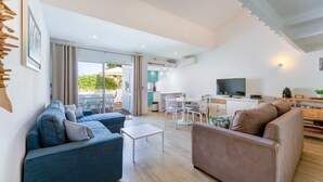 A modern living room with a sofa, a coffee table, and a TV. There is a dining area with a table and chairs, and a kitchen in the background. - Relaxing Beach House in Alfamar by LovelyStay (Olhos de Água)