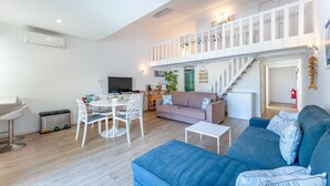 A spacious living area with a blue sofa, a dining table with chairs, a TV, and a staircase leading to an upper level. - Relaxing Beach House in Alfamar by LovelyStay (Olhos de Água)