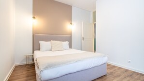 Un letto ben rifatto con testiera grigia, biancheria da letto bianca e un piccolo comodino con una lampada.