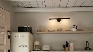 A compact kitchen with a white refrigerator, a microwave, a coffee maker, a toaster, and a sink with a faucet. There is a wooden countertop and a shelf above the sink. - Palace Modern Residences at the Railyard - Studio (Santa Fe)