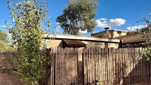 A wooden fence with a gate, a tree, and a building with a brown awning in the background. - Palace Modern Residences at the Railyard - Studio (Santa Fe)