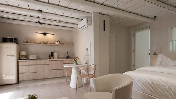 A modern bedroom with a bed, a chair, a small table, and a kitchenette area. - Palace Modern Residences at the Railyard - Studio (Santa Fe)