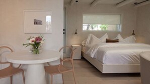 A bedroom with a bed, a bedside table with a vase of flowers, and a window.