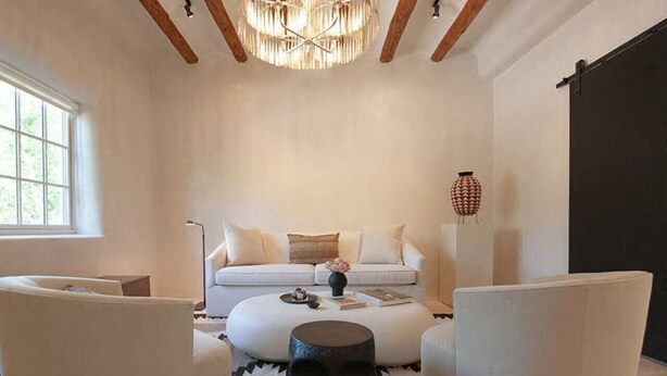 A modern living room with a white sofa, two white armchairs, a round coffee table, and a unique skull sculpture centerpiece.