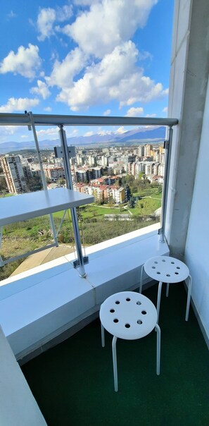 Varanda com vista para a cidade, dois bancos brancos e guarda-corpo de metal.