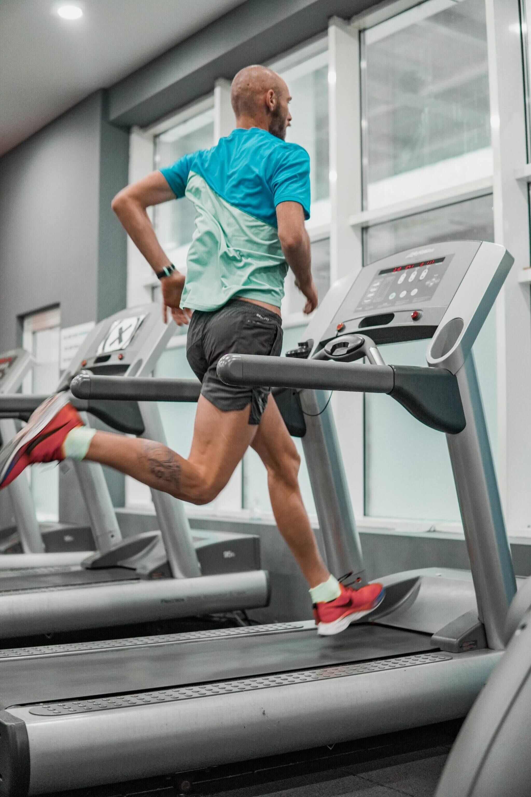 A person running on a treadmill in a gym with large windows and a modern design.