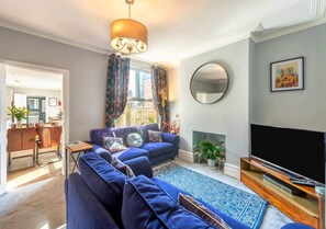 Ein Wohnzimmer mit einer Sofagarnitur, einem Flachbildfernseher, einem Kamin und einem Essbereich, der durch eine offene Tür sichtbar ist.