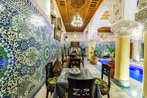 Un comedor con una pared de baldosas estampadas, una araña y una piscina al fondo.