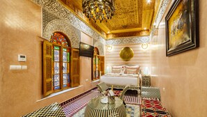 Una habitación con diseños intrincados en las paredes y el techo, una cama con almohadas, un televisor y un reposapiés estampado.